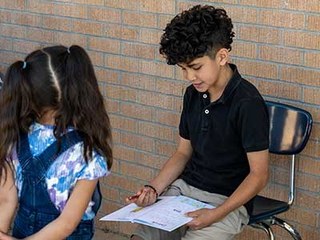 elementary student reading a worksheet to another student