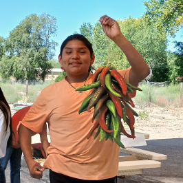 Color JPEG of Indigenous Knowledge Keeper student holding chile ristra. 