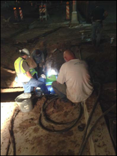 Three M&O employees repairing the water line by the light of a flashlight