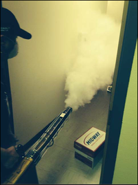 An M&O employee wearing a gas-mask, fogging a room