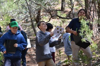 Kids smiling and doing tree key activity in the woods Students doing Tree Key at the SMNHC during their Ecology Field Experience.