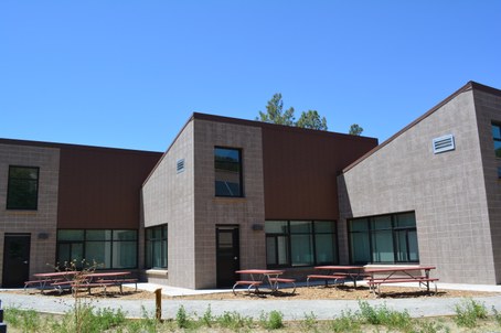Brown building with 3 separate classrooms connected on angles and picnic tables outside