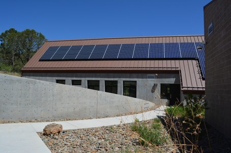 Cement building with solar panels across roof and windows on side, sidewalk curving toward