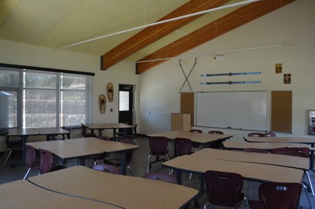 Classroom with long tables, chairs, whiteboard, skis and snowshoes on walls, and wooden ceiling beams