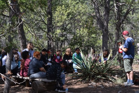Students and adults sitting on half circle of benches with yuccas in front and adult and student standing in front