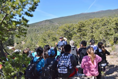 Students sitting at benches facing instructor standing with mountain view behind