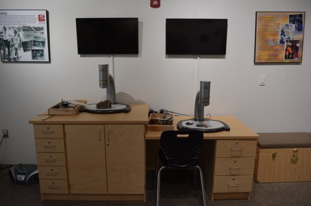Two desks with microscopes, specimens, and two tv screens above