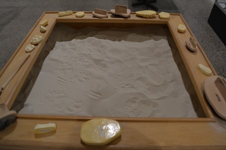 Wooden table with open middle pit filled with sand and track casts along border