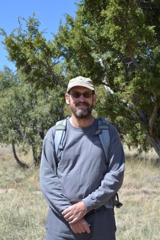 Volunteer Michael standing in front of some juniper trees and smiling at the camera