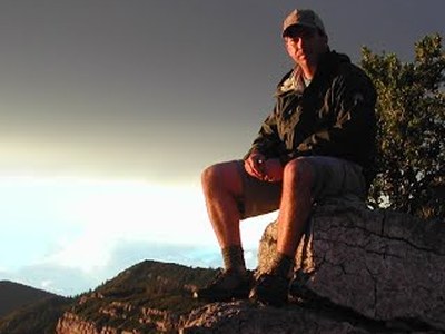 SMNHC Director Paul Mauermann sitting on a rocky cliffside at sunset