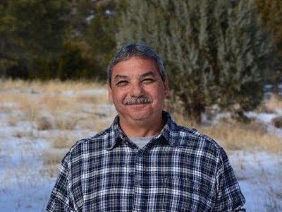 SMNHC Maintenance Worker Toby Archuleta smiling in front of snowy field and trees.