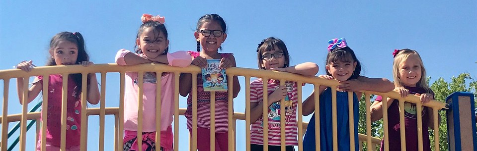 Six students smiling while standing on playground equipment.