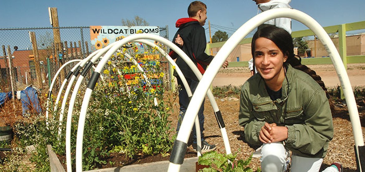 Middle school student sitting outside next to school garden.