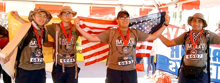 Four JROTC Navy students in a group, celebrating a race finish by holding a JROTC flag
